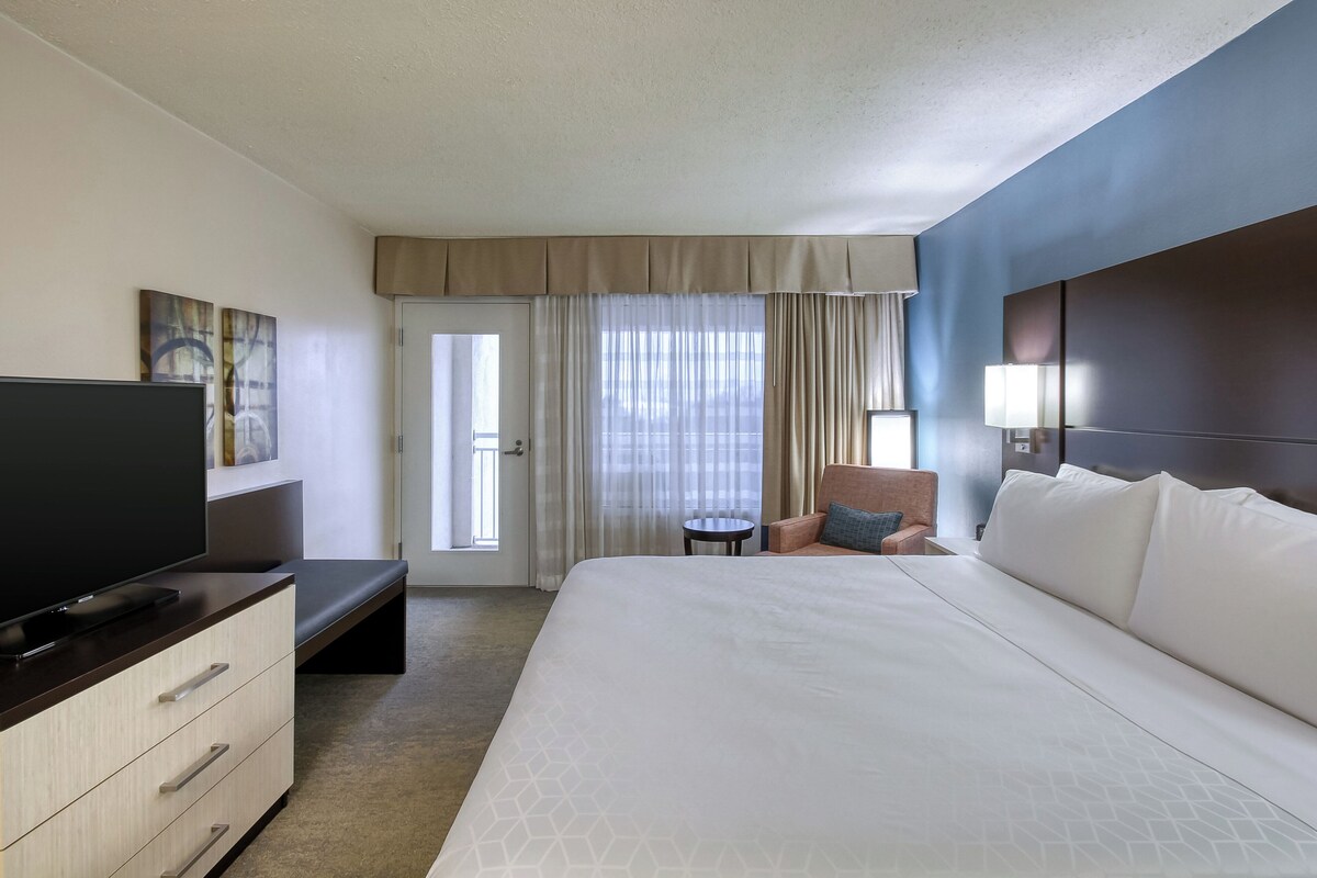 A hotel room with a bed, a TV, a desk, a chair, and a window with curtains.