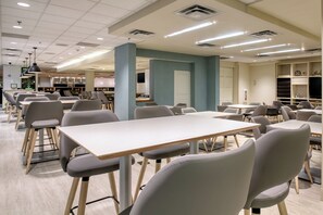 A modern dining area with tables and chairs, a kitchen in the background, and a blue accent wall. - Holiday Inn Hotel & Suites Atlanta Airport-North by IHG (Atlanta)