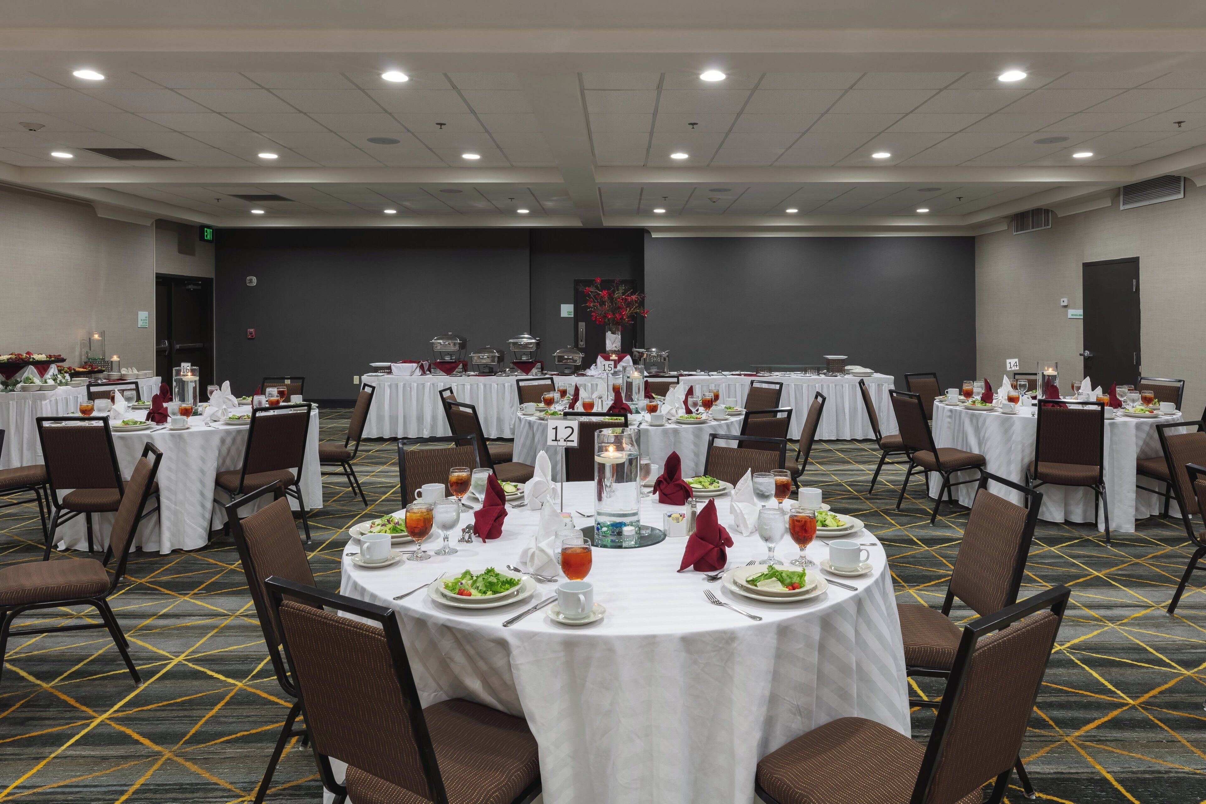 Sala de conferências com mesas redondas, cadeiras e estações de buffet.