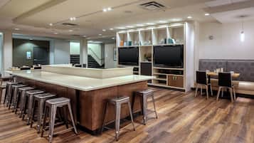 Een moderne bar met een centraal bar eiland, barstoelen en een zithoek met een bank en fauteuils.