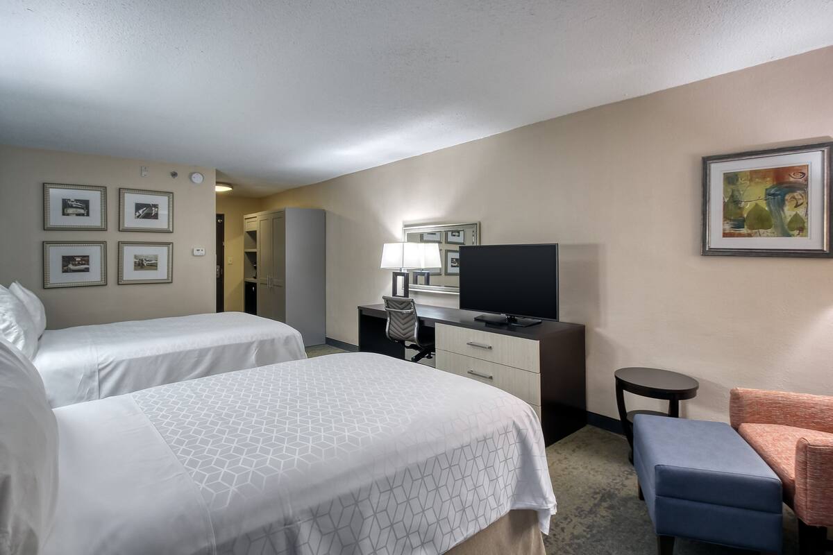 A hotel room with two beds, a desk with a chair, a television, and a small table.