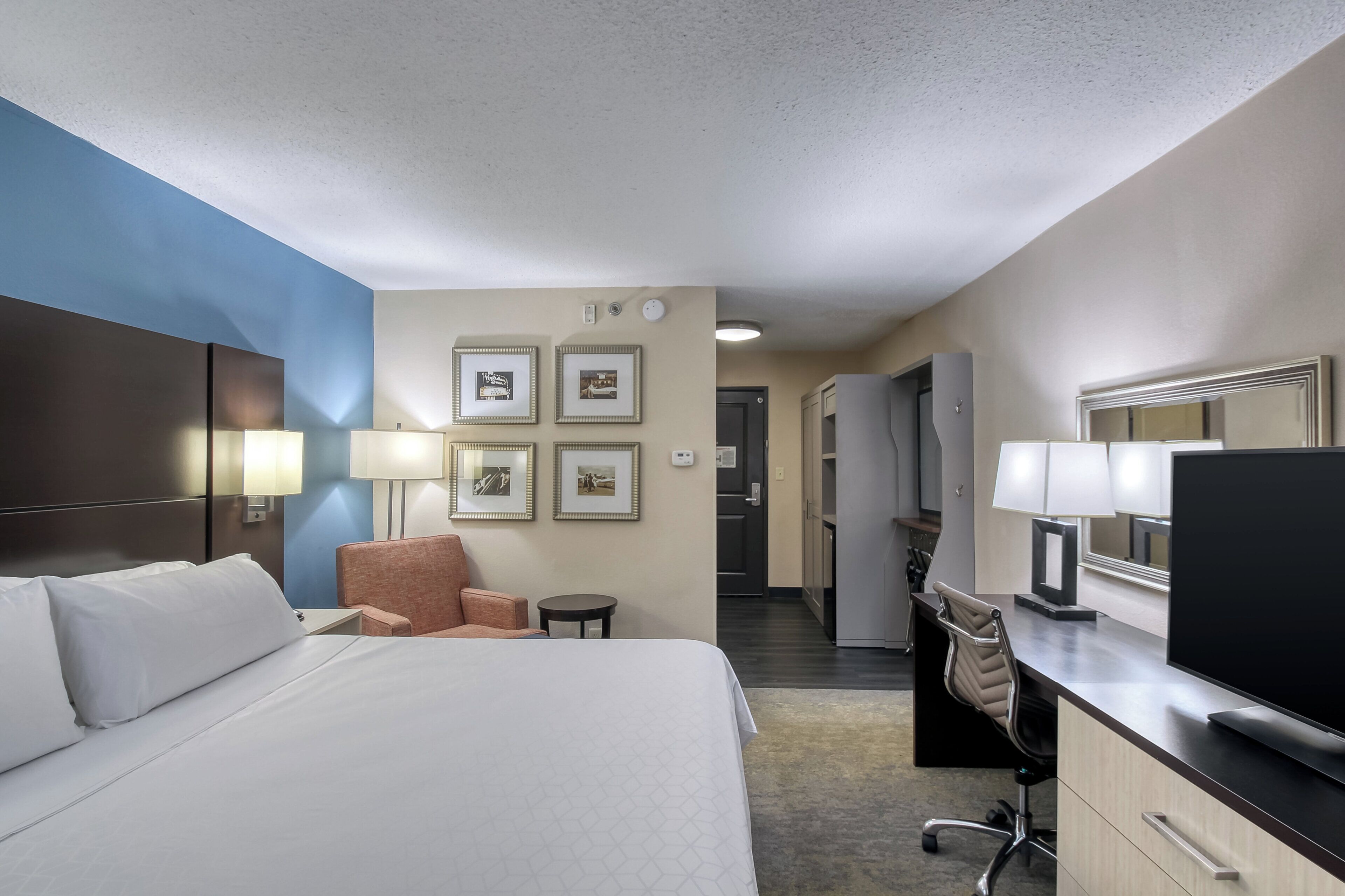 A hotel room with a bed, desk, chair, TV, and framed pictures on the wall.