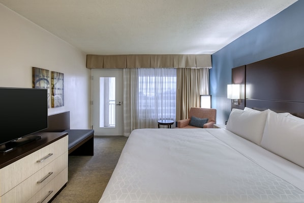 Quarto de hotel com uma cama grande, televisão, escrivaninha e uma cadeira.