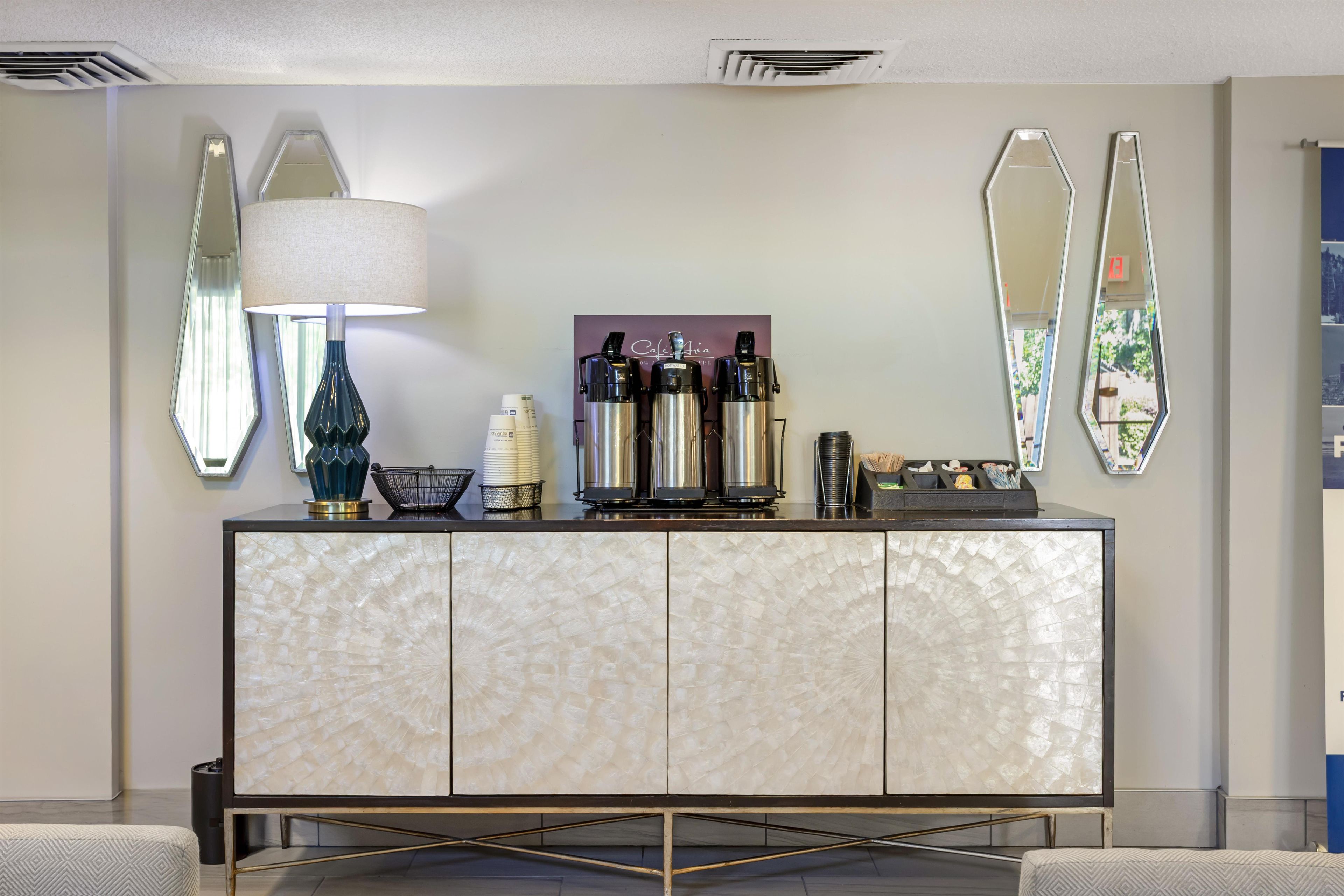 Un moderno vestíbulo de hotel con una recepción de mármol, una máquina de café y espejos decorativos.