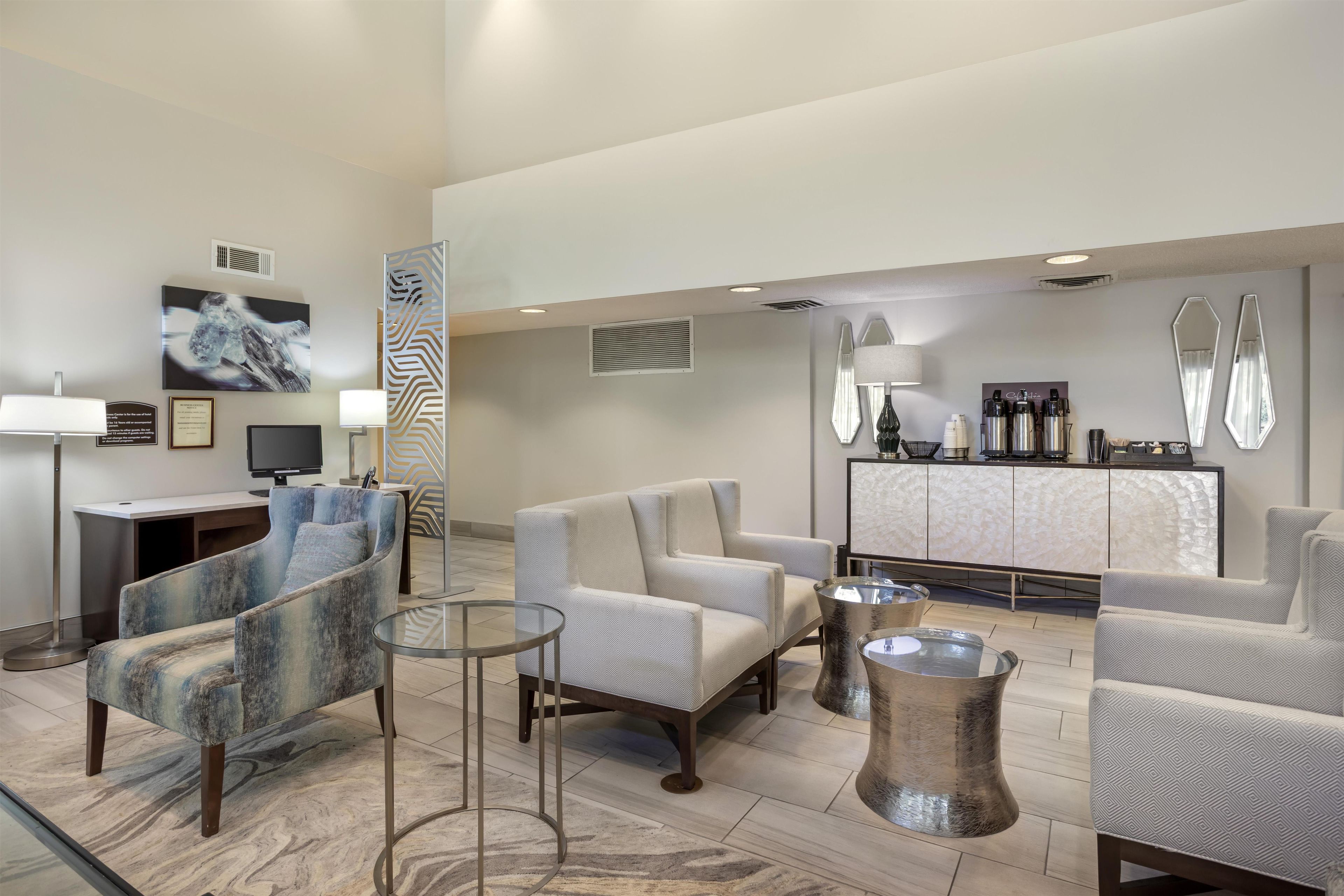 A modern hotel lobby with seating, a reception desk, and a coffee station.