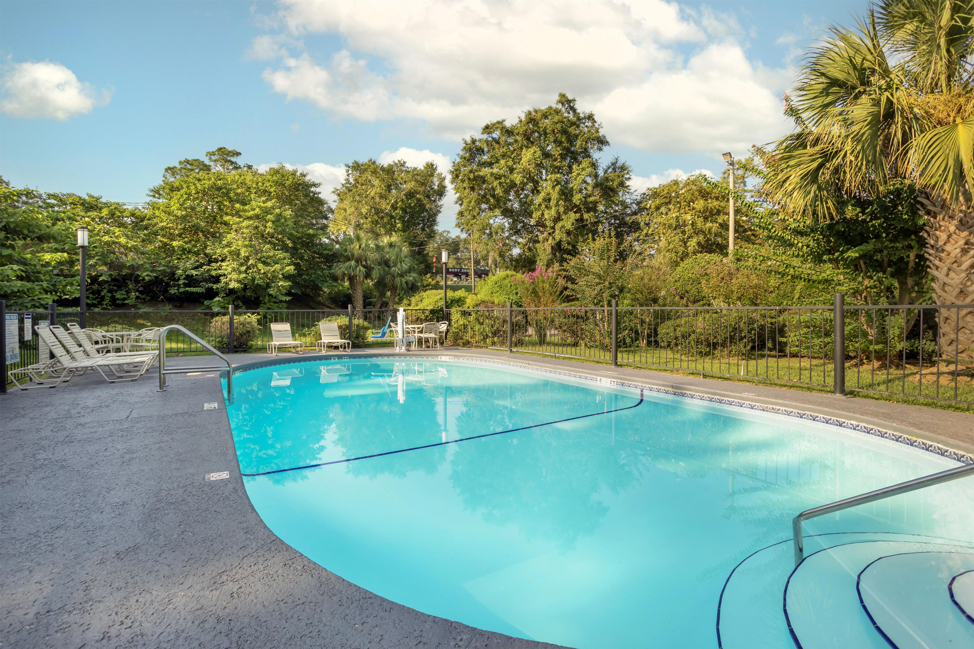 Una piscina de borde curvo, rodeada por una valla y con sombra de árboles.