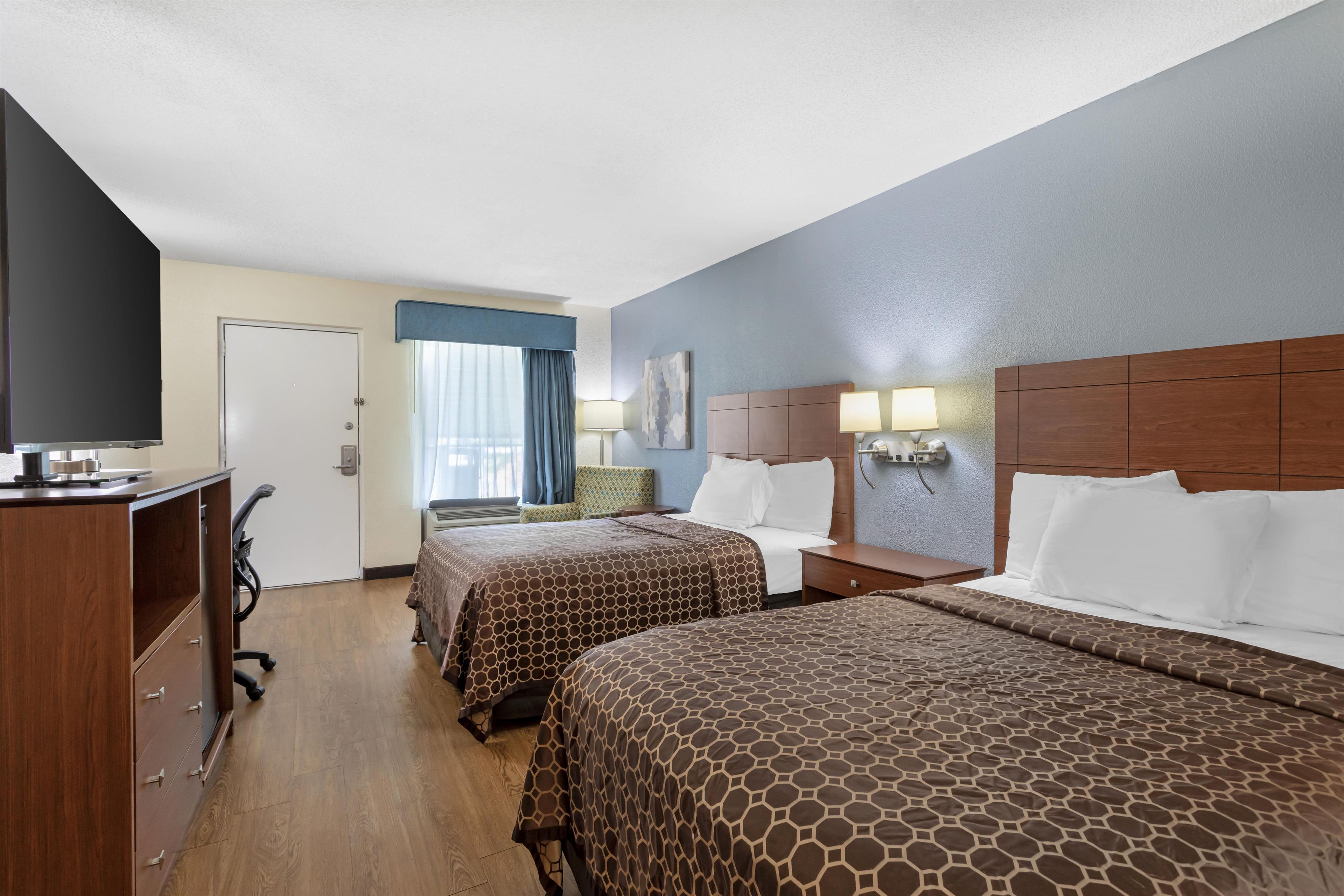 A hotel room with two beds, a desk, a chair, and a television.