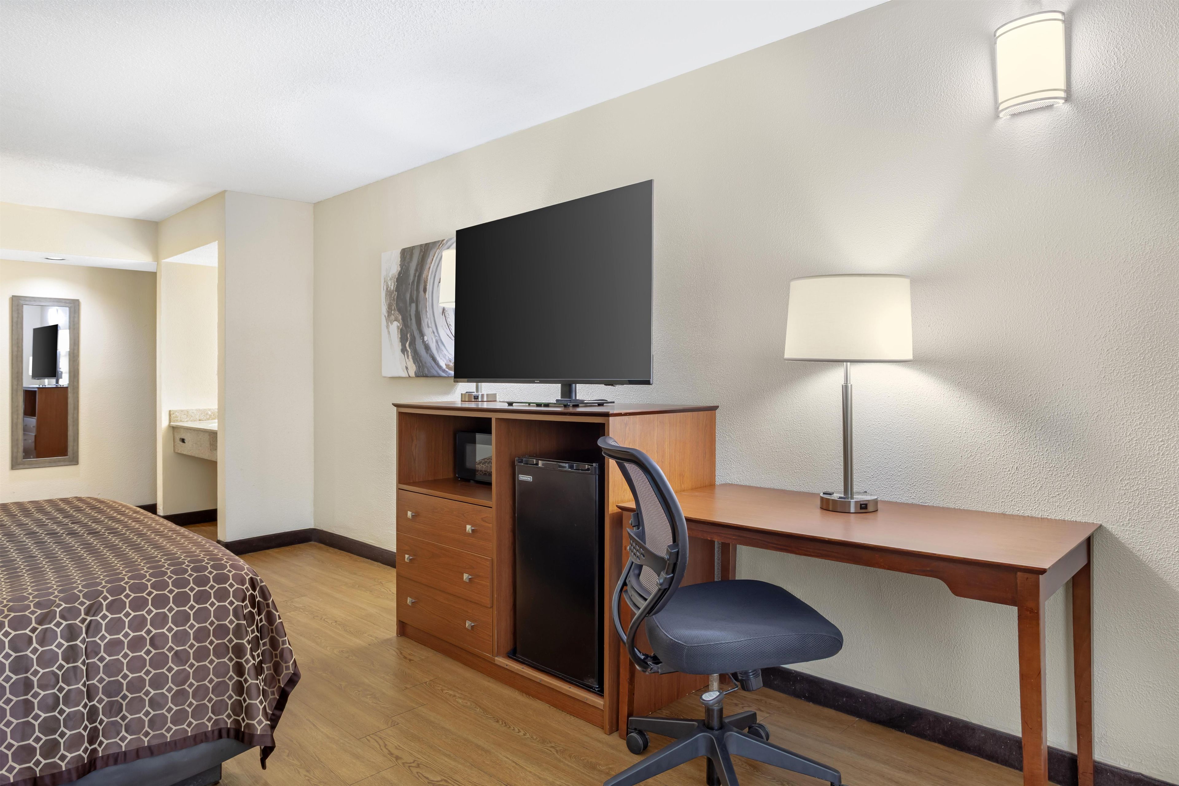 Ein Hotelzimmer mit Bett, Schreibtisch mit Stuhl, Fernseher, Lampe und Mikrowelle.