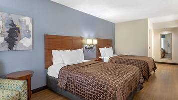 A hotel room with two beds, a small table, a chair, and a painting on the wall.