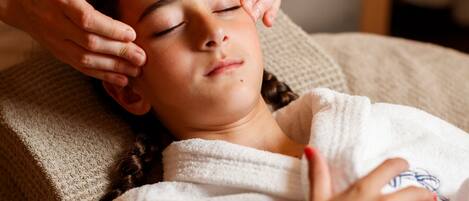 A person lying on a bed with a white blanket, receiving a head massage.