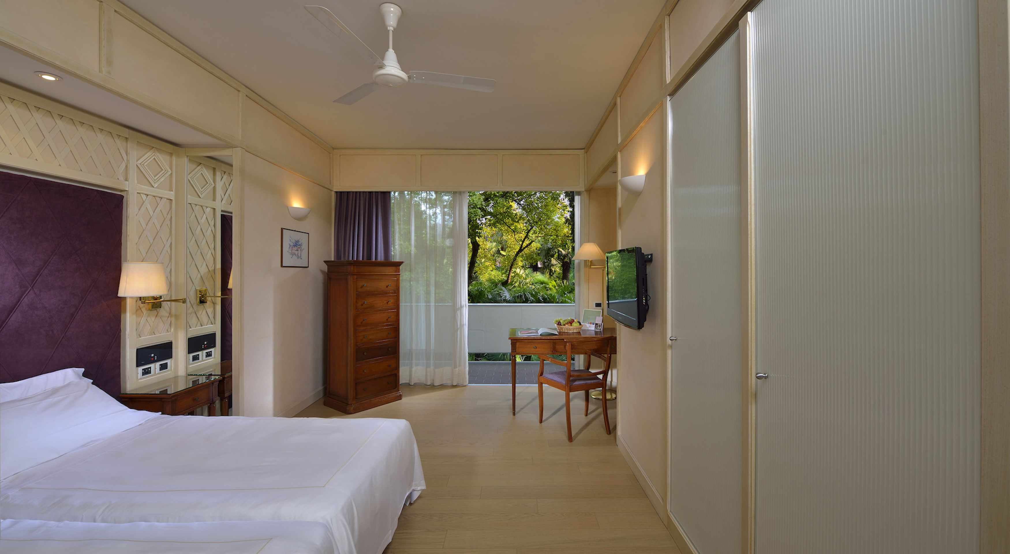 A hotel room with a bed, a desk with a chair, a television, and a wardrobe.