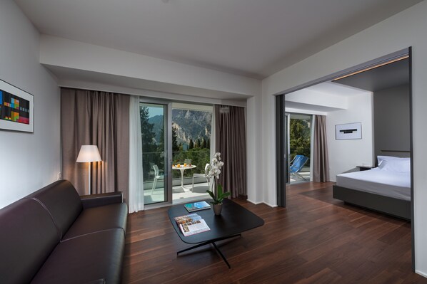 Una habitación de hotel moderna con una cama, un sofá, una mesa con una revista, una lámpara y vistas al exterior.
