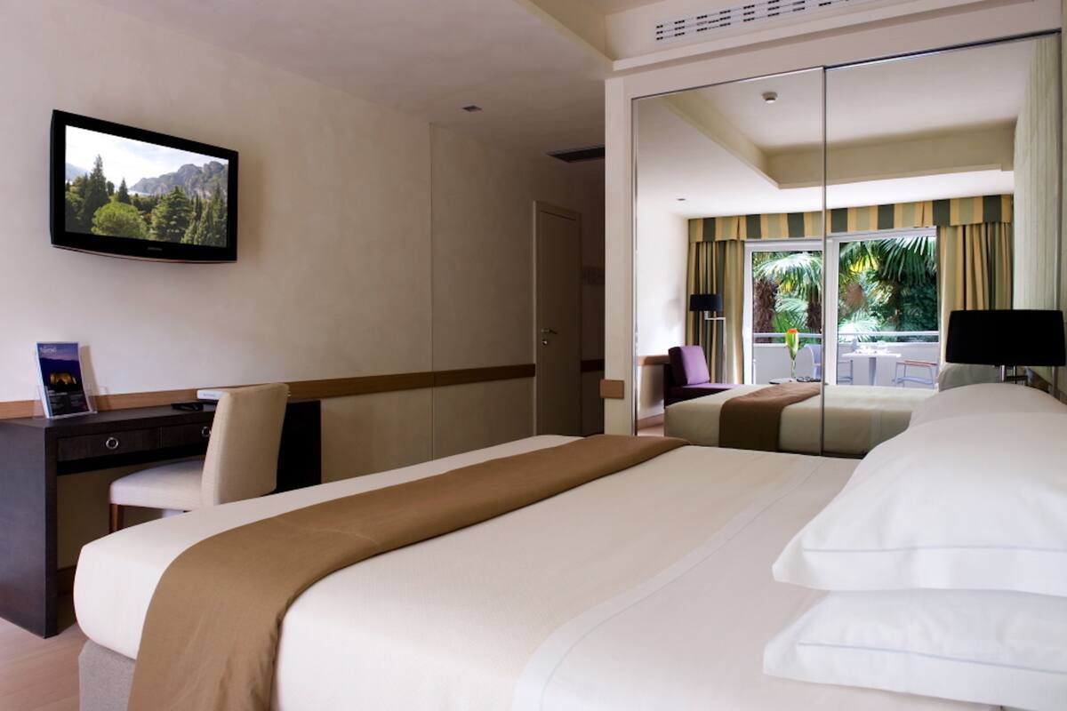 A hotel room with a bed, a desk, a chair, a television, and a sliding door to a balcony.