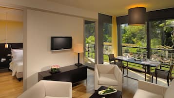 Een moderne hotelkamer met een flatscreen televisie, een nachtkastje met lamp, een bank en een zithoek met een tafel en stoelen.