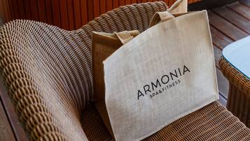 Un sofá de mimbre con un cojín color beige y una bolsa blanca con la etiqueta 'ARMONIA SPA&FITNESS'.
