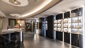 Un moderno vestíbulo de hotel con mostradores de recepción de mármol, estanterías elegantes que exhiben artículos de aseo personal y un diseño contemporáneo y limpio.