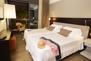 A hotel room with two beds, a desk, a chair, and a view of the outdoors.