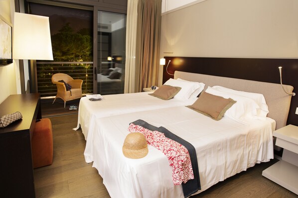 A hotel room with two beds, a desk, a chair, and a view of the outdoors.