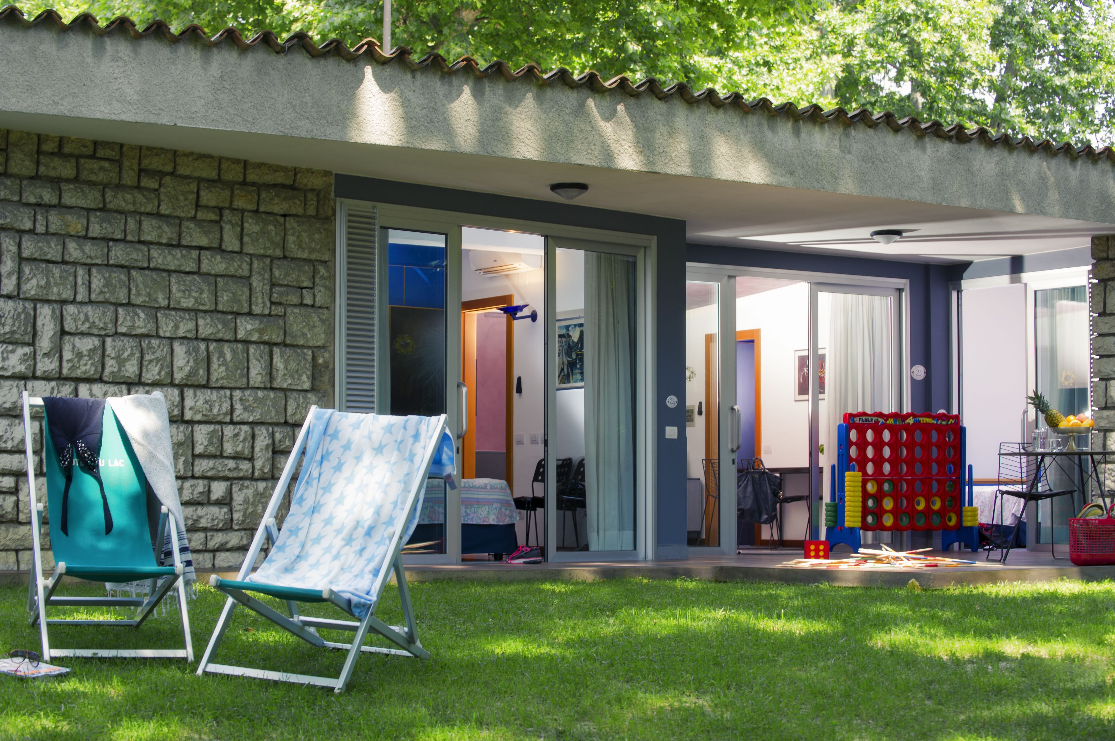 Una casa con fachada de piedra, un porche techado con sillones de jardín y una pequeña zona de juegos con juguetes y una mesa.