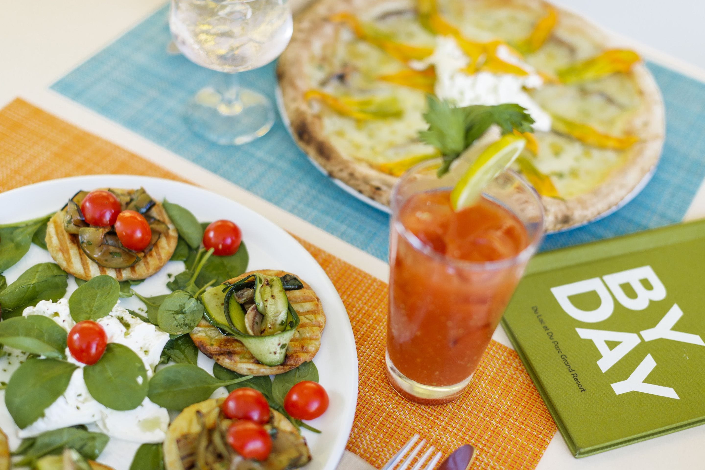 A table with a plate of grilled vegetables, a glass of iced tea, and a book titled "BY DAY".