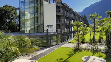 Un hotel moderno con fachada de vidrio, terraza en la azotea y un jardín bien cuidado con palmeras.