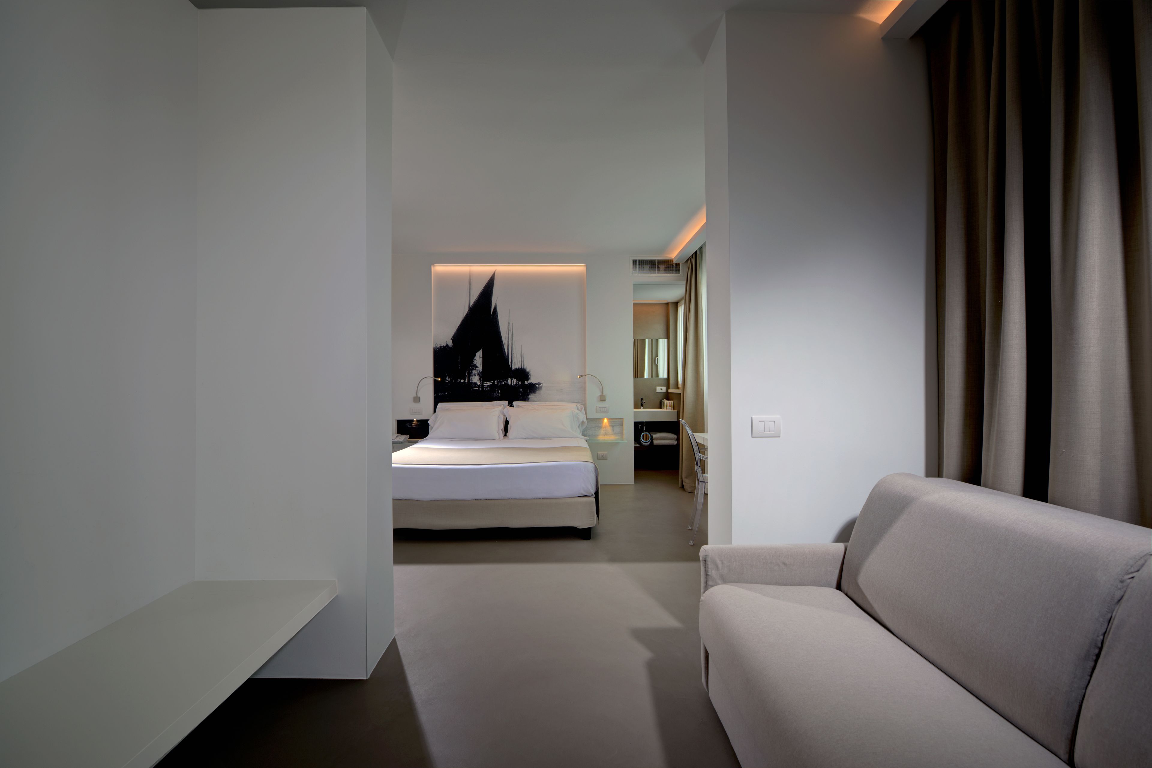 A modern hotel room with a bed, a sofa, a bathroom, and a view of the cityscape.
