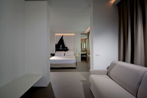Habitación de hotel moderna con cama, sofá, baño y vistas a la ciudad.