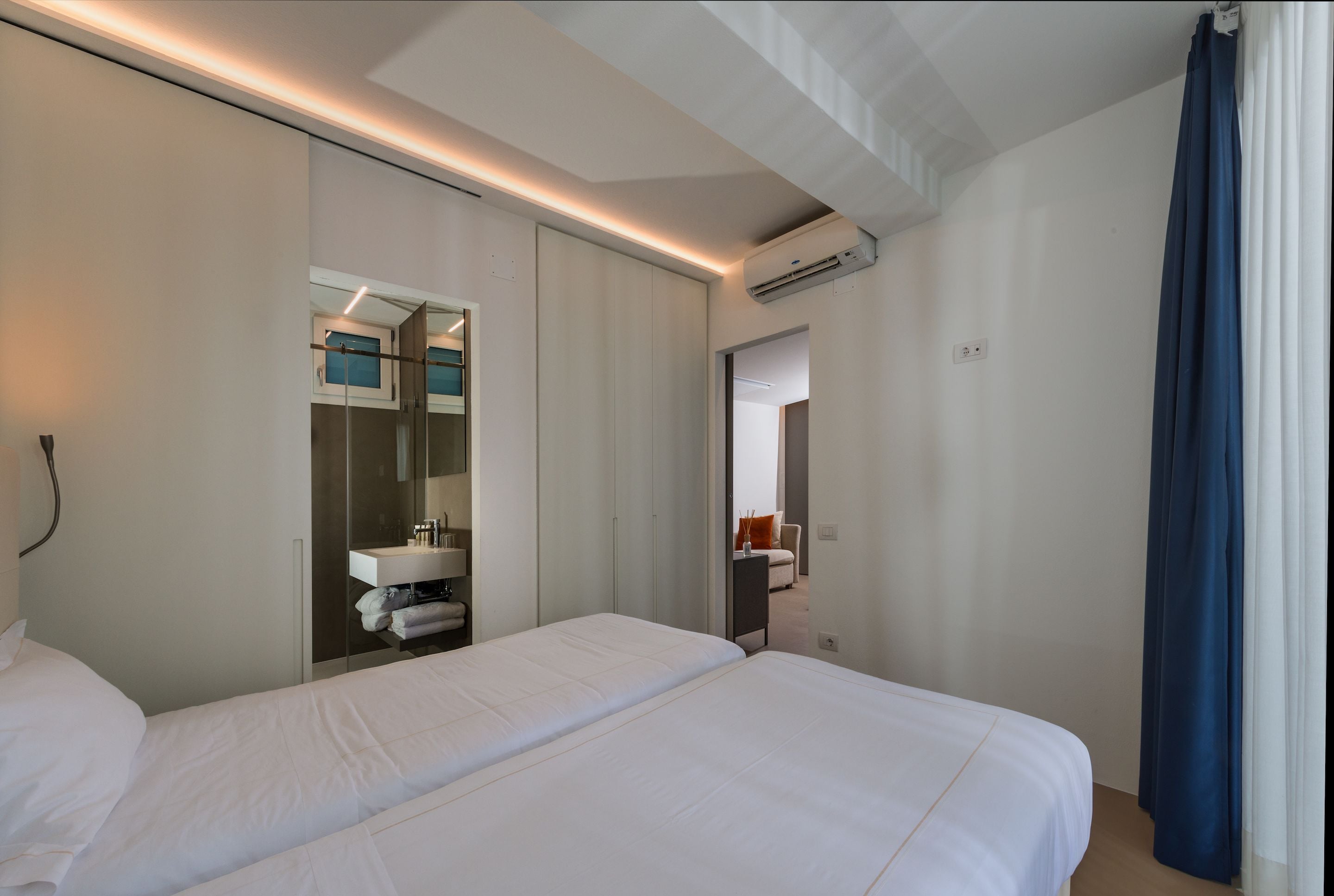 A hotel room with two beds, a bathroom with a mirror, and an air conditioning unit.