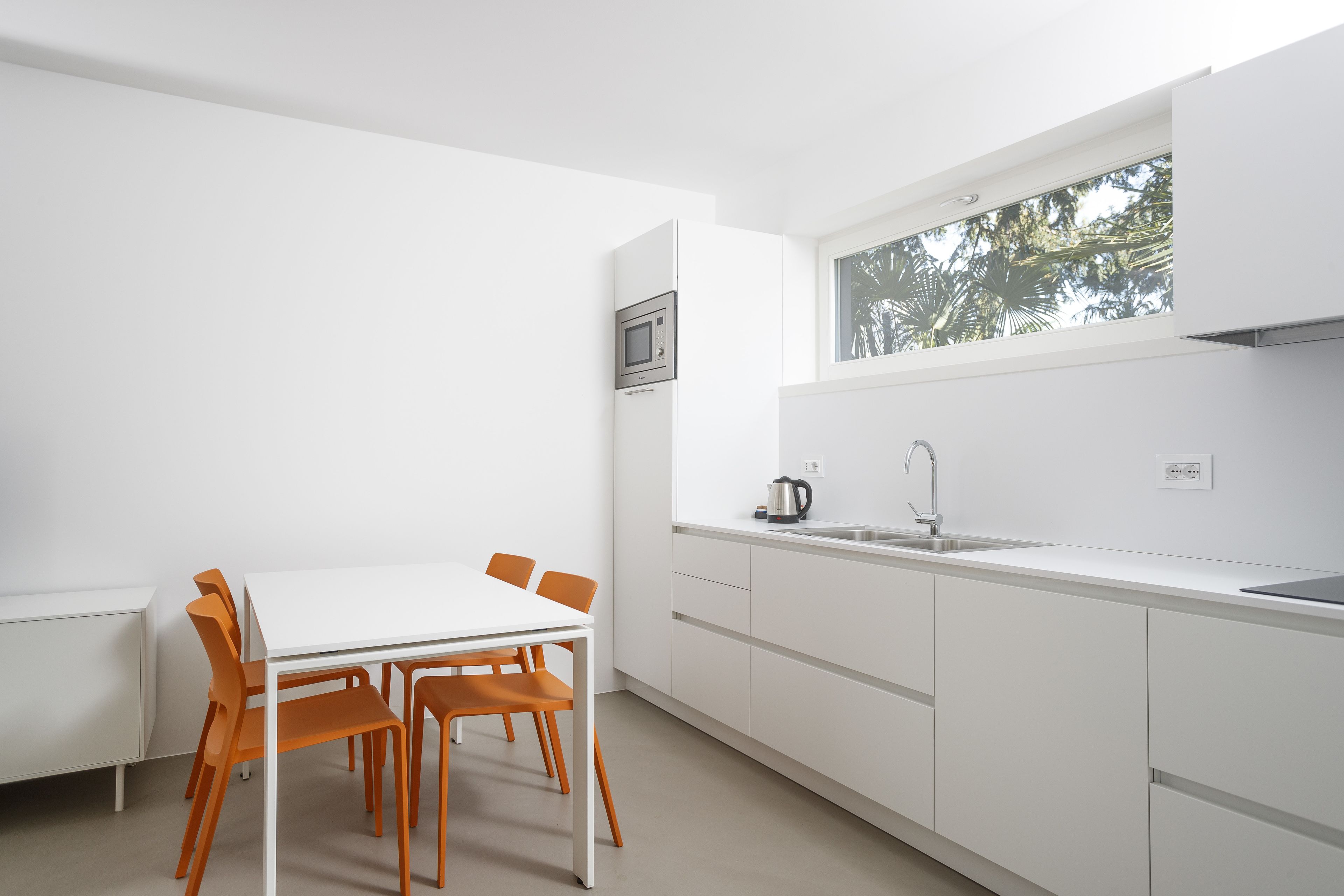A modern kitchen with white cabinets, a white countertop, and a window with a view of trees.
