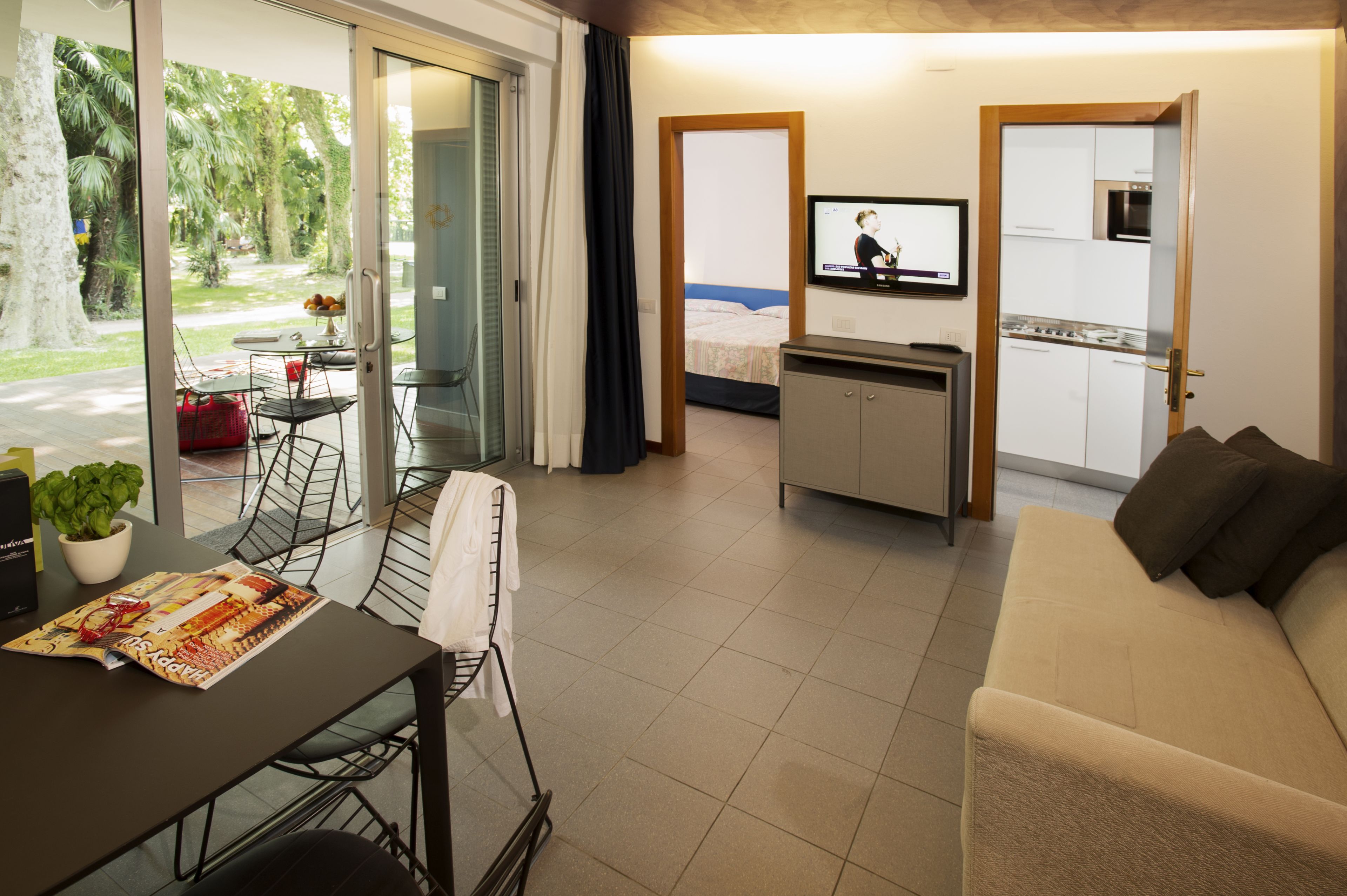 Un soggiorno moderno con un divano, un tavolo da pranzo con sedie, una TV e una zona cucina visibile attraverso un'apertura.