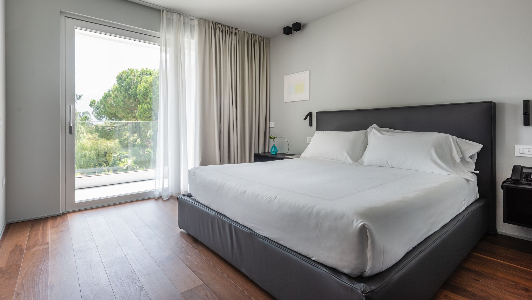 Habitación de hotel moderna con una cama grande, una mesita de noche, un teléfono y vistas a zonas verdes.