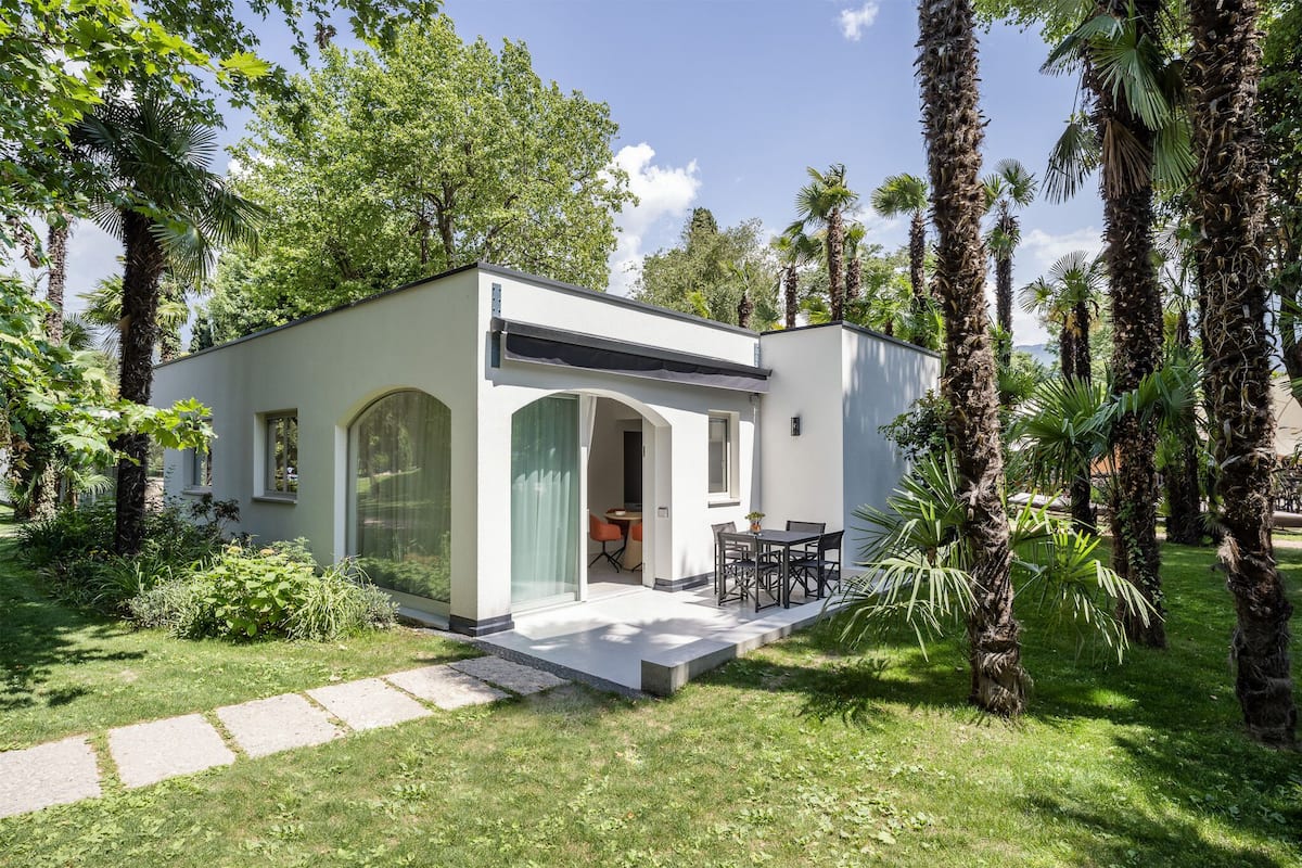 A modern house with a patio, surrounded by lush greenery and palm trees.