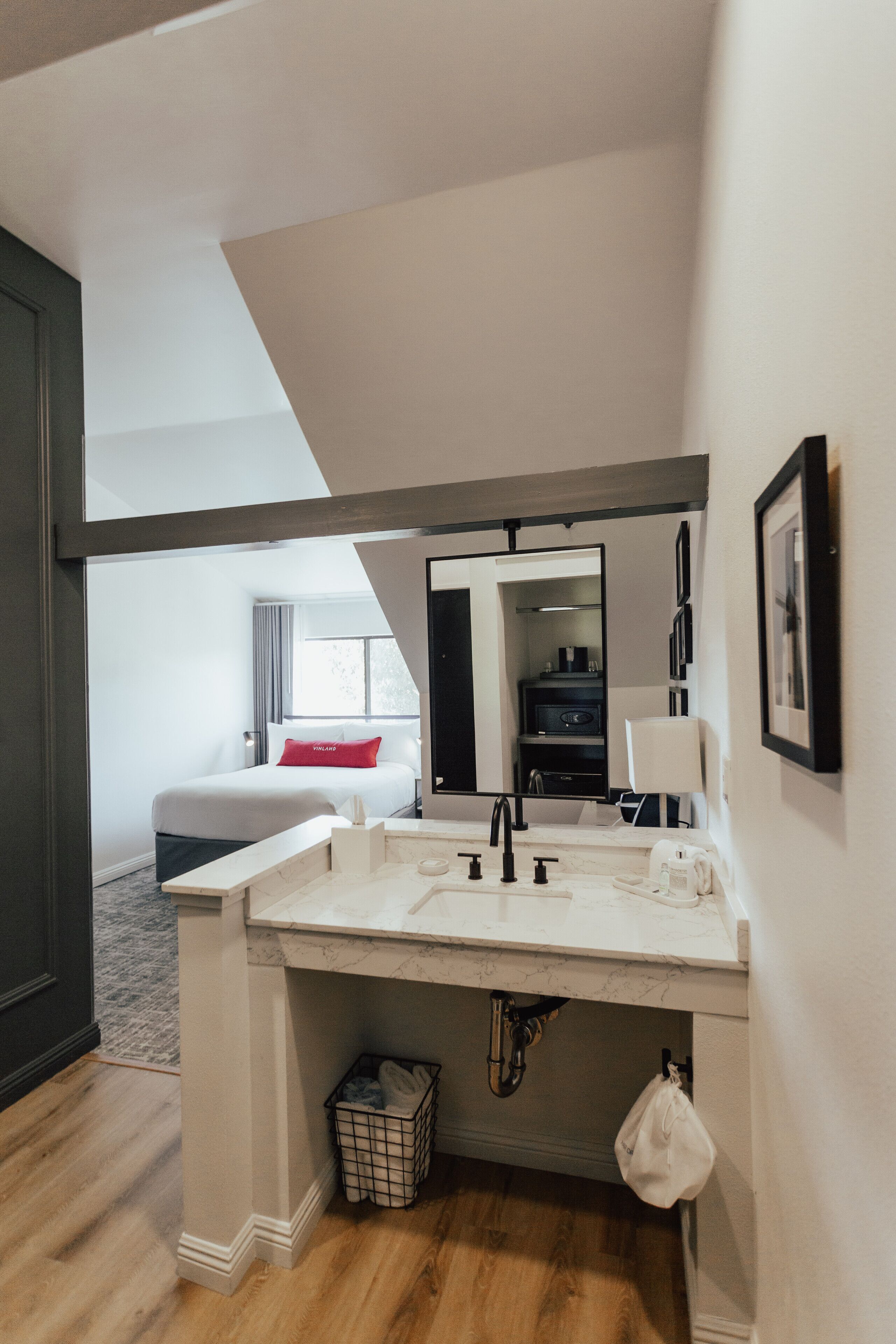 Une salle de bain moderne avec un grand miroir, un lavabo et des toilettes. On trouve une petite poubelle sous le lavabo et une serviette accrochée au mur.