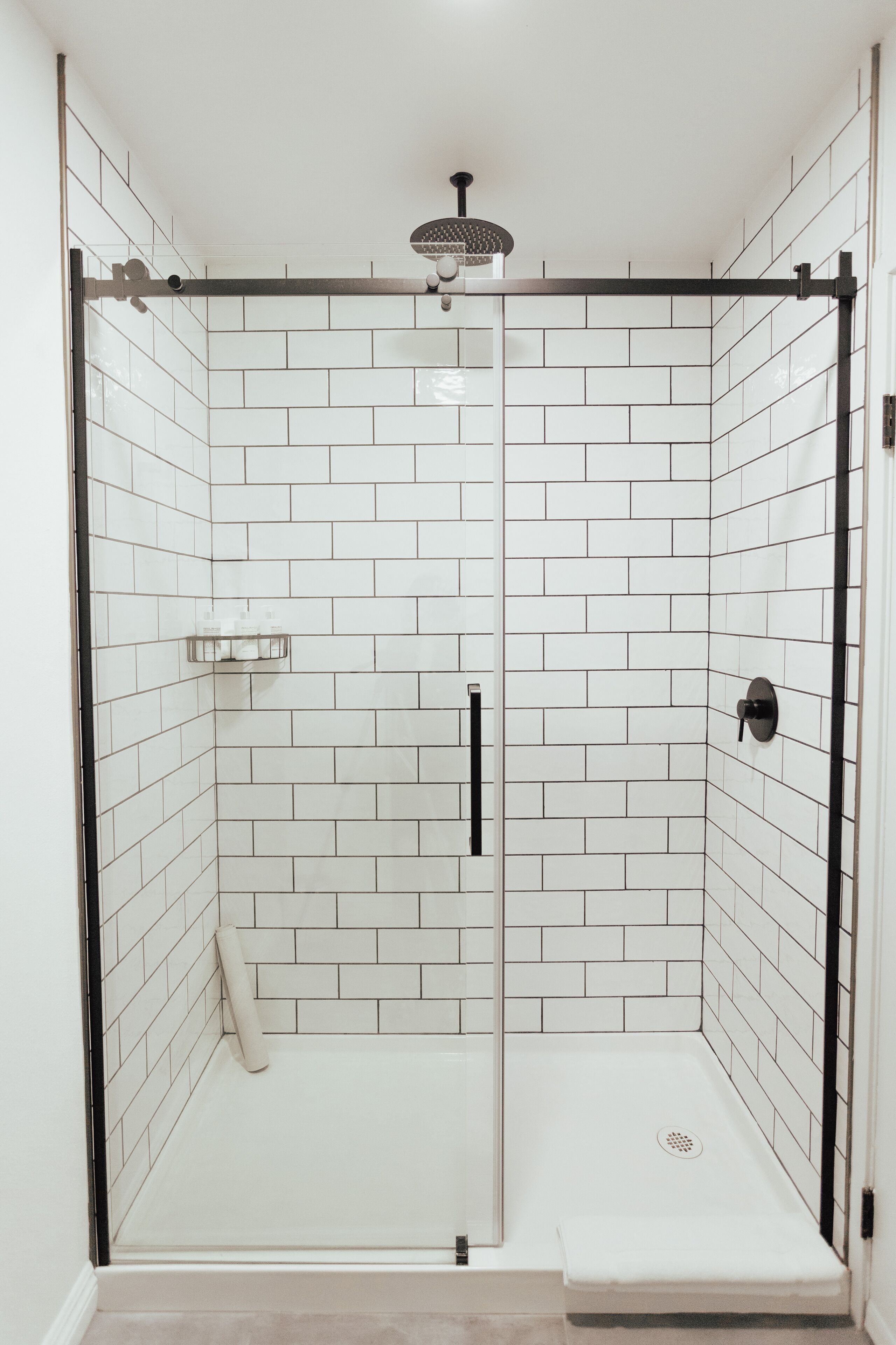 A modern shower with white tiles and a glass door.