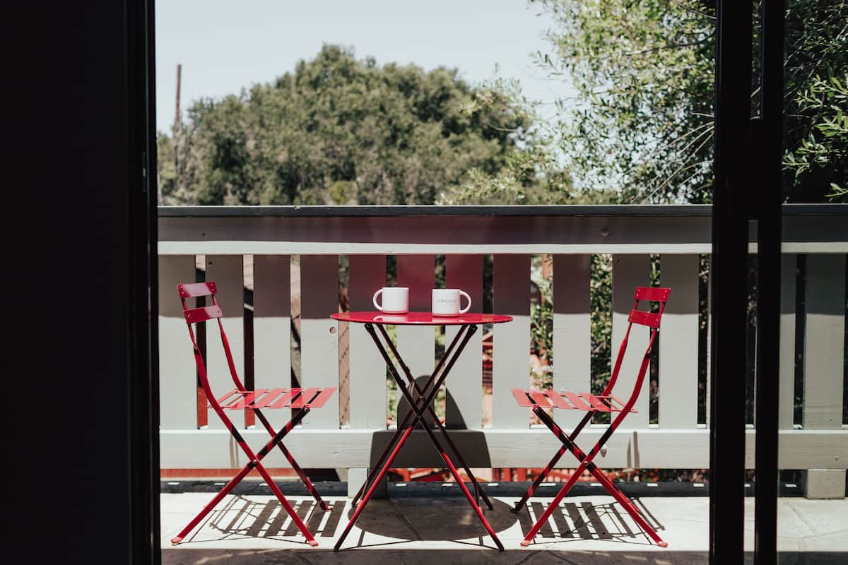 A red and white outdoor seating area with a table and chairs, a white railing, and a view of trees in the background.