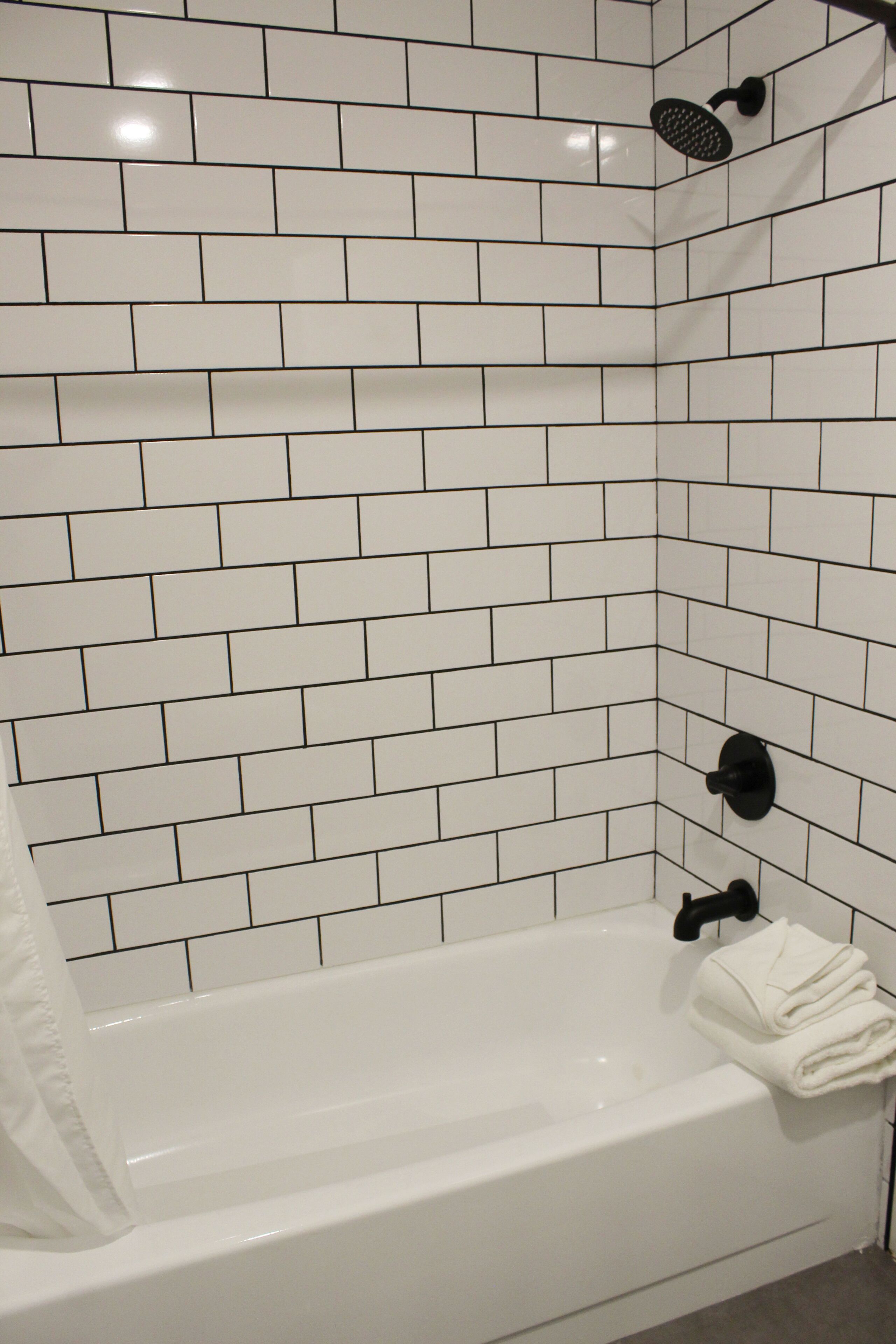 A white-tiled shower area with a black showerhead and a towel rack.
