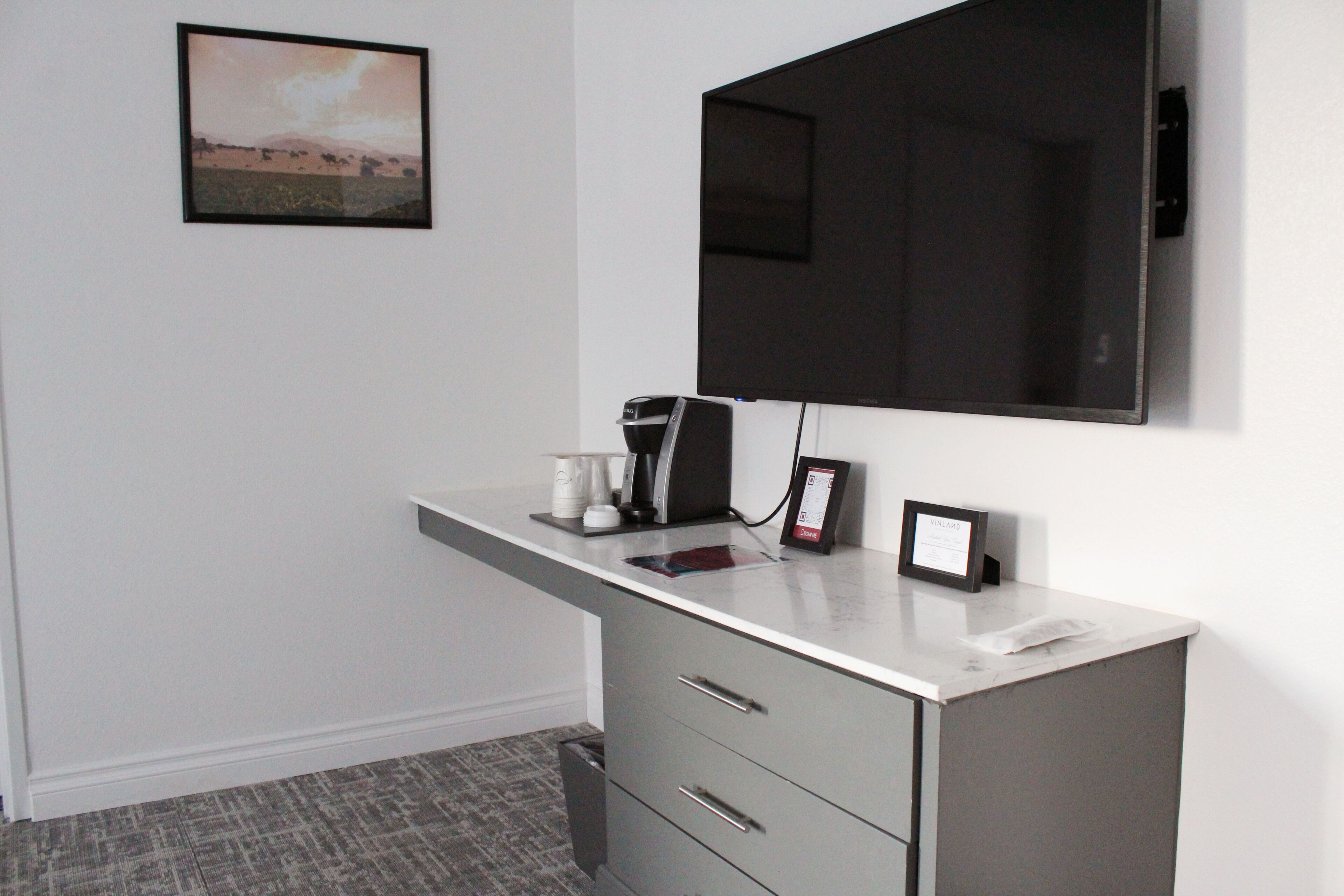 A hotel room with a marble desk, a flat-screen TV, a framed picture on the wall, and a small trash bin.