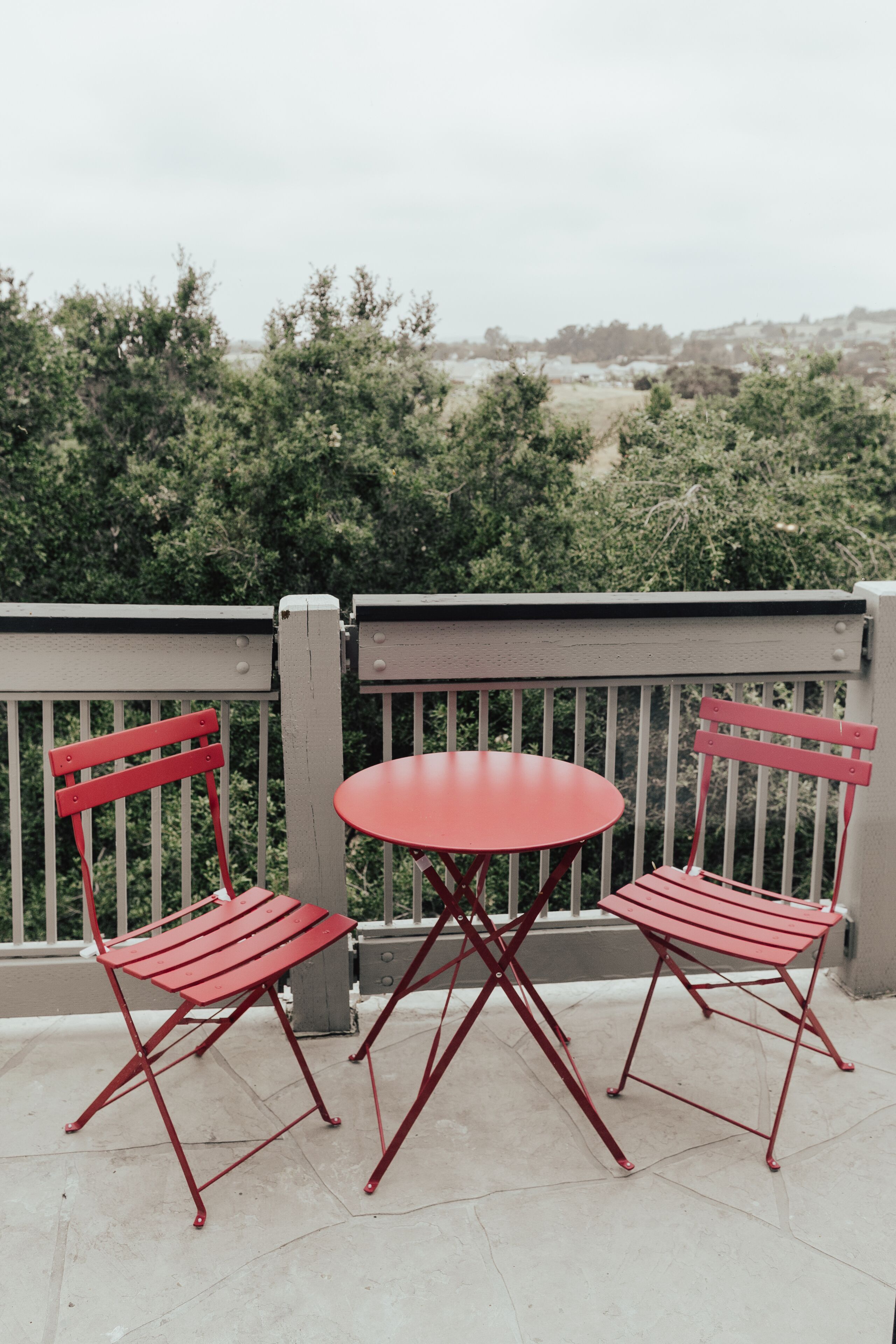 Un balcon avec deux chaises en métal rouge et une petite table ronde.
