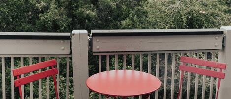 Un balcón con dos sillas de metal rojas y una mesita redonda.