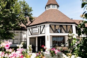 A traditional Tudor-style building with a conical roof, a sign reading "VINLAND," and a garden with various flowers in the foreground. - Vinland Hotel and Lounge (Solvang)