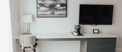 Un espacio de oficina moderno con escritorio, silla, lámpara, cafetera y un cuadro en la pared.