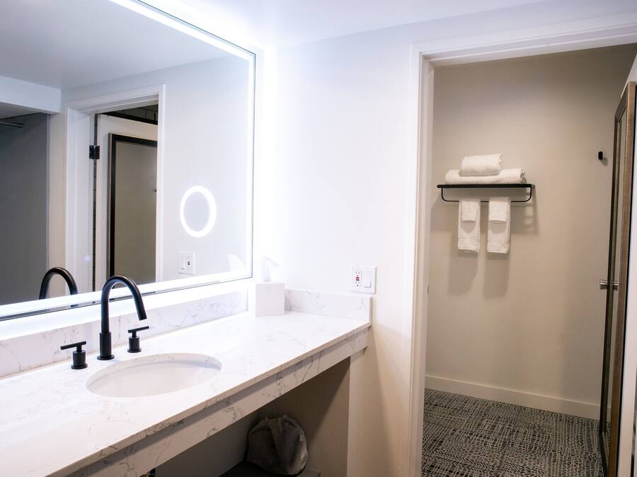 A bathroom with a white marble sink, black faucets, a large mirror, and a towel rack.