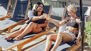 Two lounge chairs with a wooden frame and a dark cushion, positioned under a black umbrella.