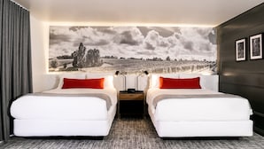 A hotel room with two beds, a large wall mural, and a nightstand with lamps.