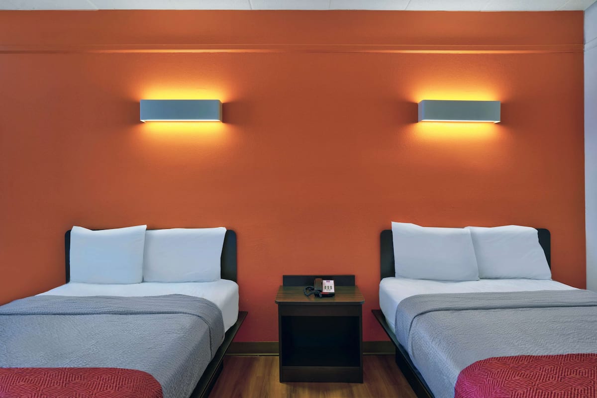 A hotel room with two beds, a nightstand with a phone, and wall-mounted lights.
