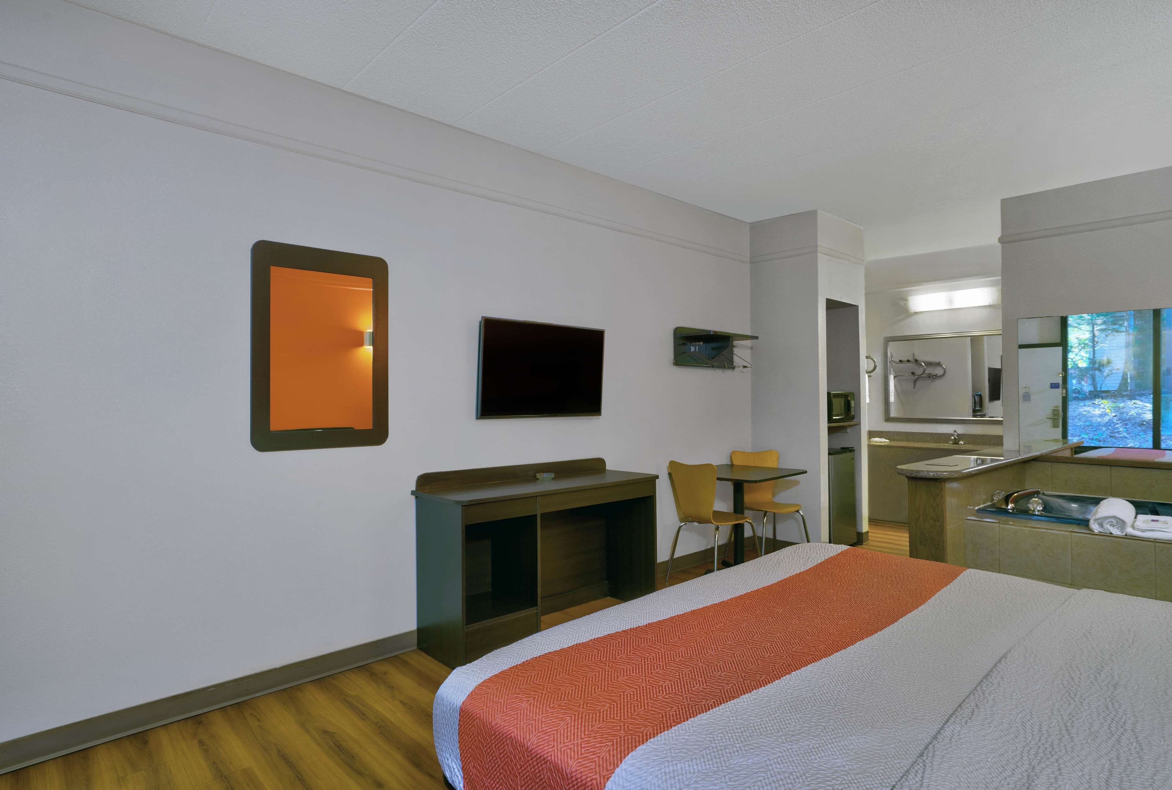 A hotel room with a bed, a desk, a chair, a TV, and a bathroom with a sink and mirror.