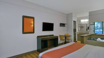 A hotel room with a bed, a desk, a chair, a TV, and a bathroom with a sink and mirror.