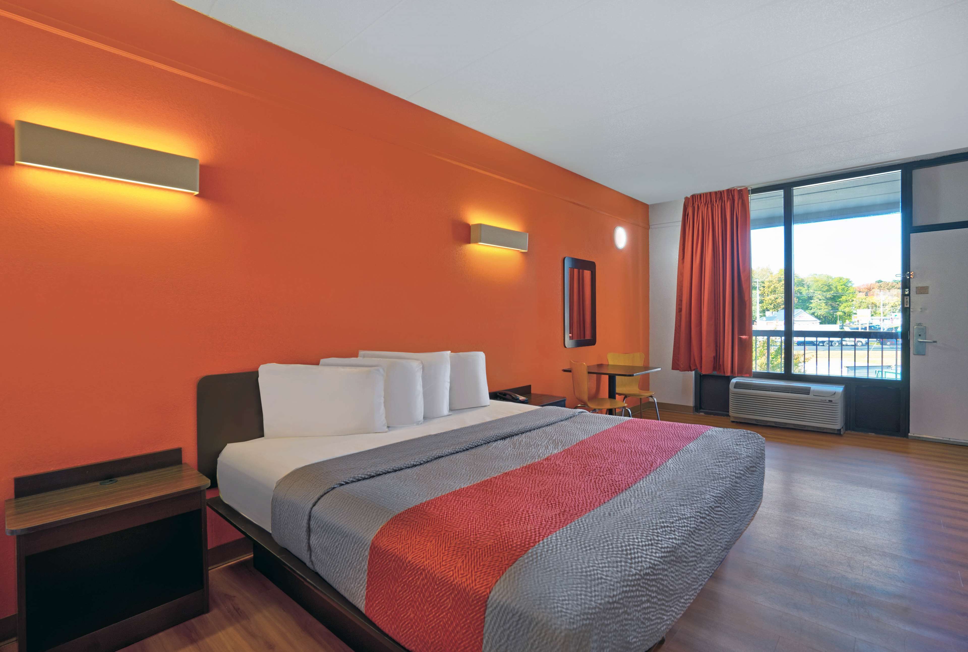 A hotel room with a large bed, orange walls, a window with a view, and a desk with a chair.