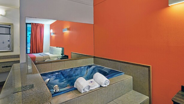 Un baño moderno con una bañera grande, un espejo y una pared de color naranja brillante.