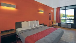 Habitación de hotel con una cama grande, dos mesitas de noche, un escritorio y una silla. Hay dos luces fijadas a la pared y una ventana con cortinas.